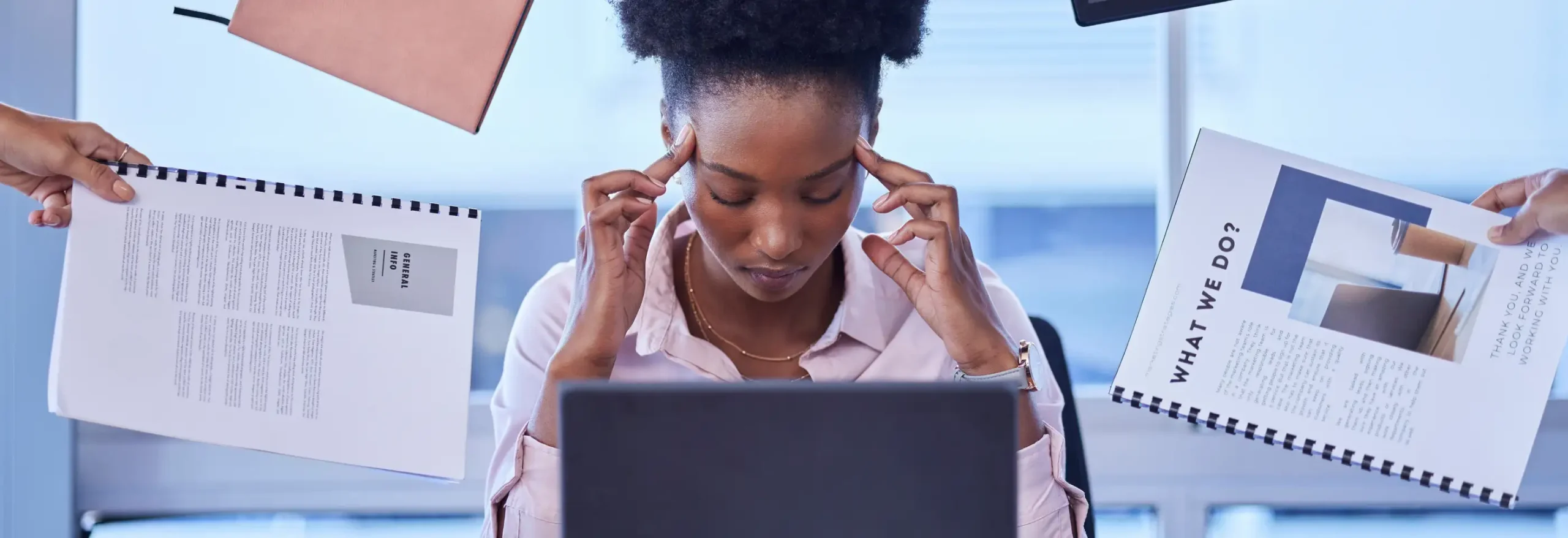 Focused professional at laptop as multiple documents and binders are handed from both sides