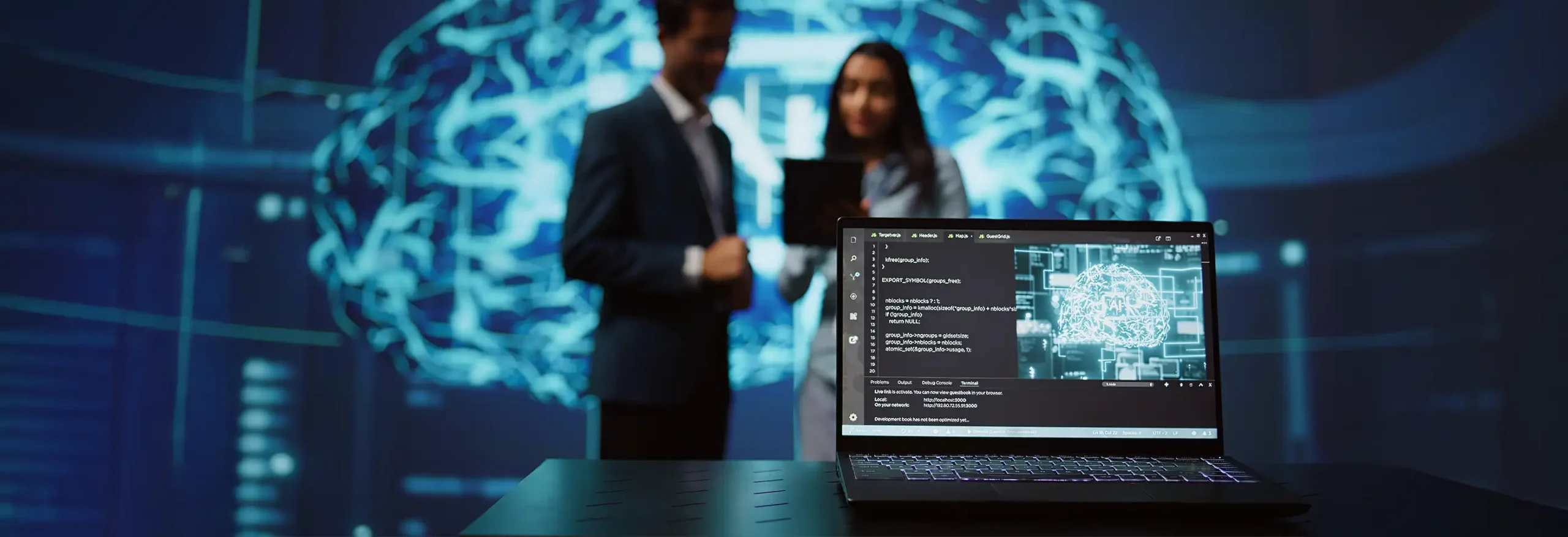 Laptop with code and digital brain on desk while two professionals view glowing neural network projection in background